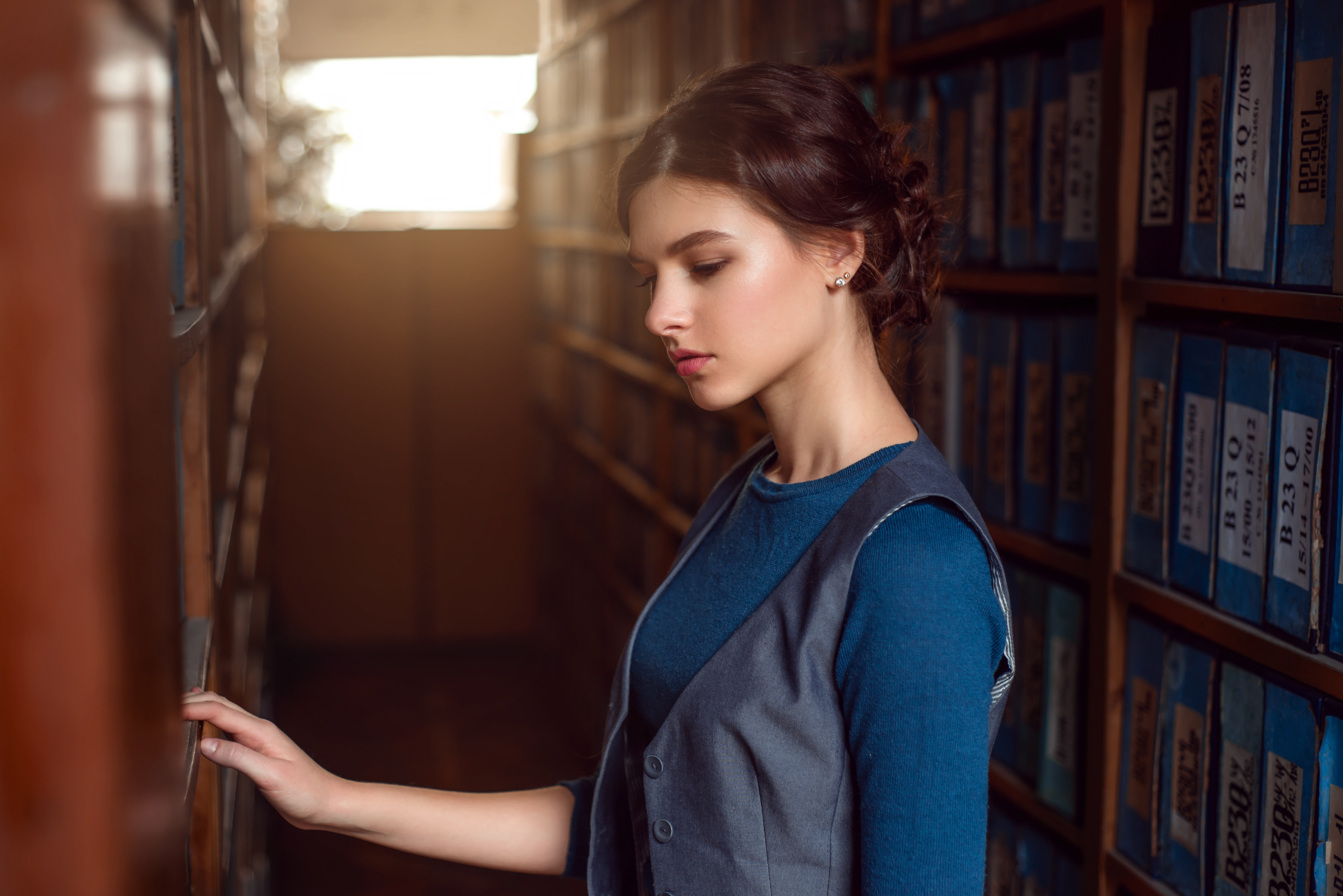 Young woman selecting book from library shelf.